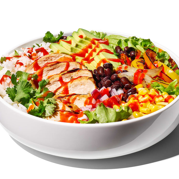 A white bowl filled with a colorful salad with chicken, avocado, corn, black beans, and red onion.
