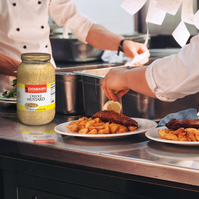 A jar of Zatarains Creole Mustard sits on a counter next to a plate of fried food.