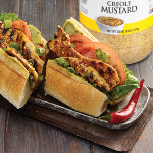 A close-up of a Creole Mustard sandwich with grilled chicken, avocado, tomato, and green onions.