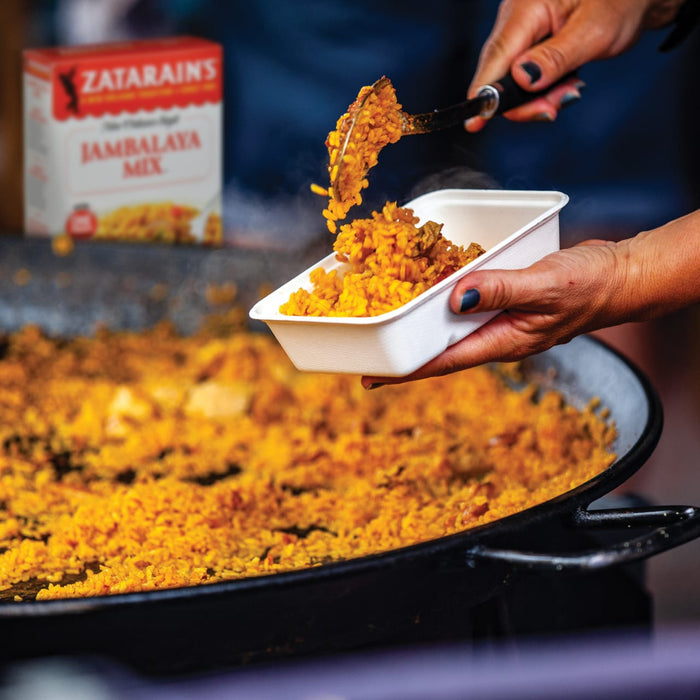 A hand is serving a portion of Zatarains Jambalaya Mix into a white container.
