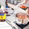 A bottle of Zatarains Shrimp &amp; Crab Boil sits on a table next to a pot of boiling crawfish.