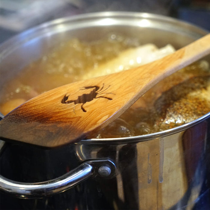 A wooden spoon with a crab carved into it rests on top of a pot of boiling water.