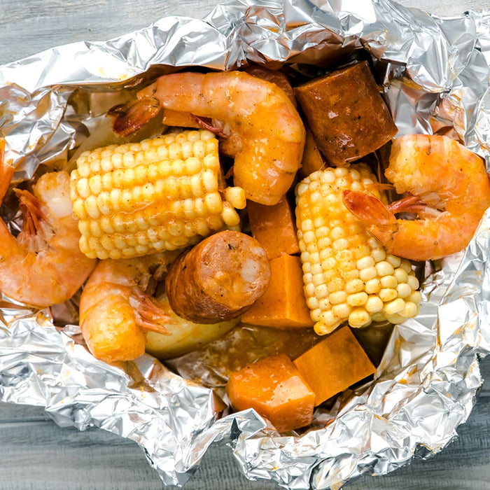 A foil packet filled with shrimp, corn on the cob, sausage, and sweet potatoes.
