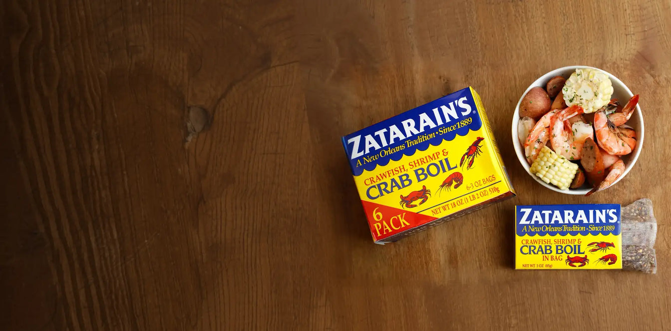 Zatarain's Crawfish, Shrimp & Crab Boil 6-pack and single bag next to a bowl of boiled shrimp, corn, and potatoes