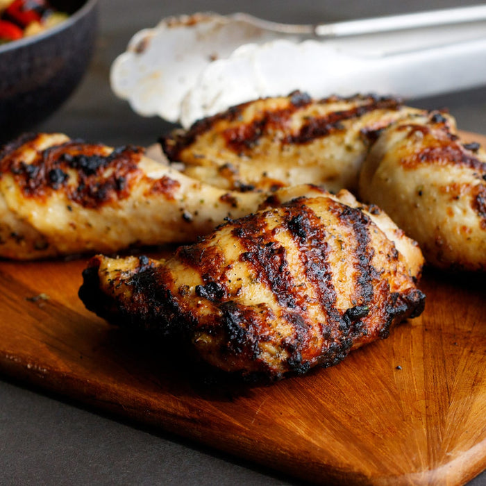 Grilled chicken pieces on a wooden cutting board.