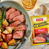 A plate of cooked meat with potatoes and asparagus next to a package of Adolphs Marinade in Minutes.