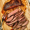 A wooden cutting board with a fork and sliced grilled steak.
