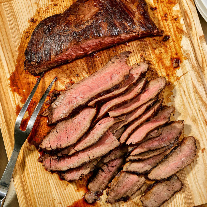 A wooden cutting board with a fork and sliced grilled steak.