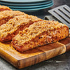 Three pieces of salmon crusted with breadcrumbs are on a wooden cutting board.