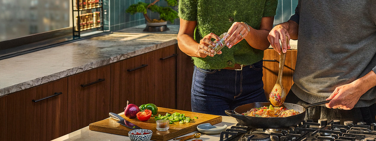 Two people cooking together in a kitchen with various ingredients and utensils.