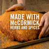 A hand sprinkles McCormick herbs and spices on a large piece of meat.