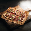 A flatbread pizza topped with pulled pork and red onions is seasoned with Mccormick Culinary White Pepper Ground 80 Oz and garnished with fresh cilantro and crushed peanuts on a rustic wooden board.