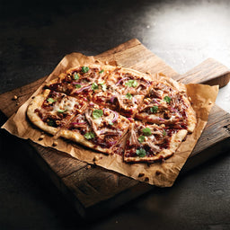 A flatbread pizza topped with pulled pork and red onions is seasoned with Mccormick Culinary White Pepper Ground 80 Oz and garnished with fresh cilantro and crushed peanuts on a rustic wooden board.