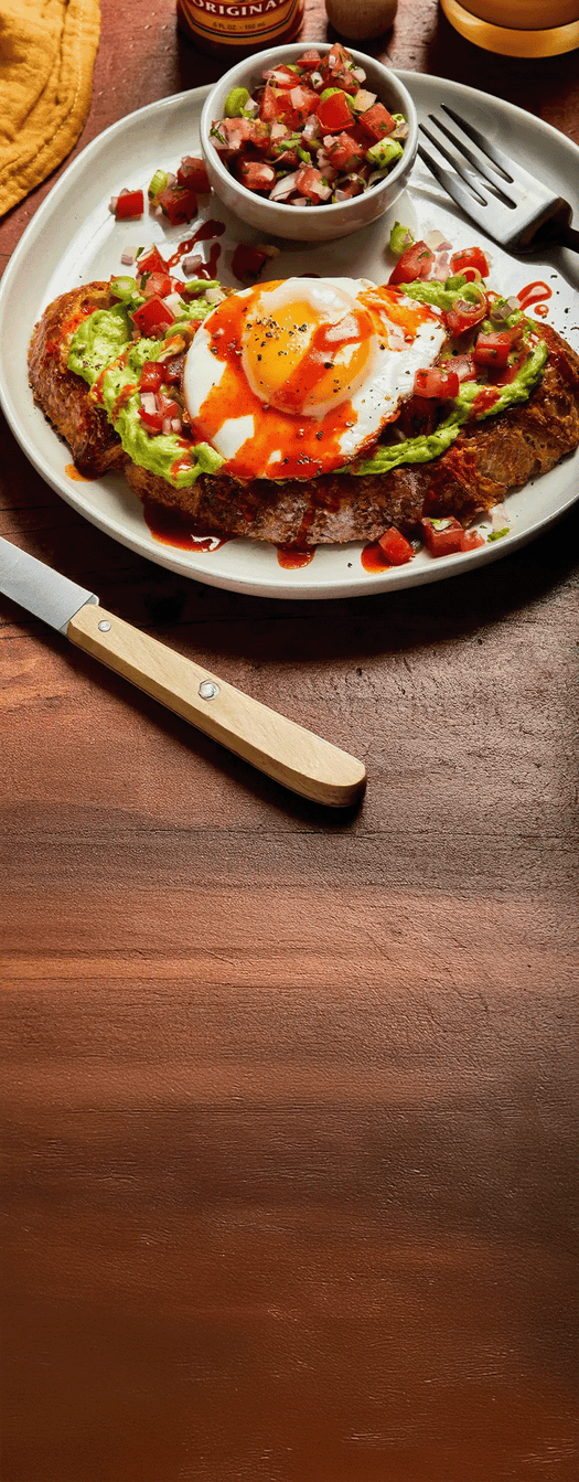 Plate of food with a sunny-side-up egg, avocado, and tomato on a wooden table.