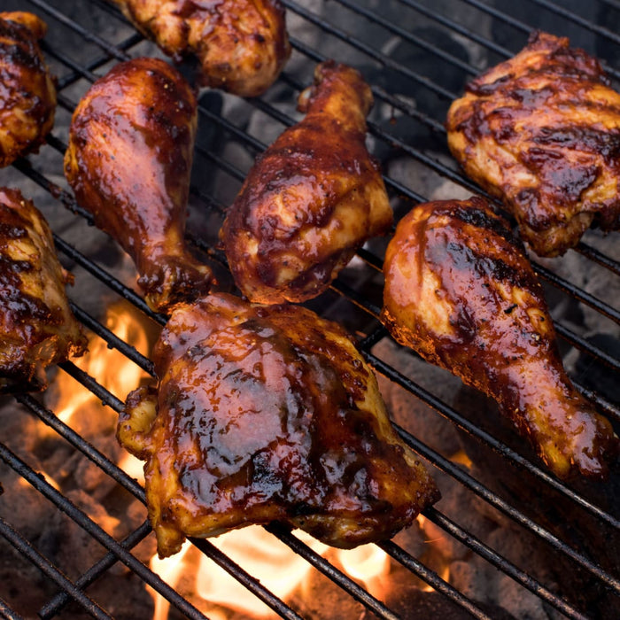 Barbecue chicken pieces are cooking on a grill over a bed of hot coals.