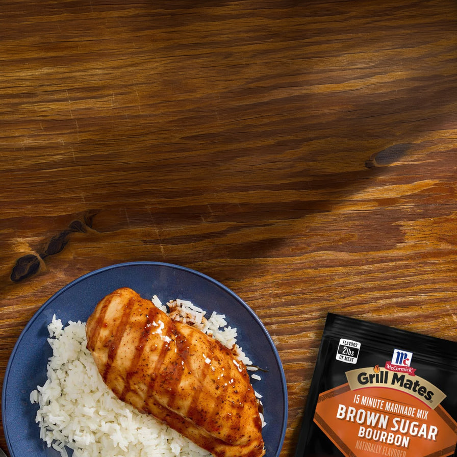 Grilled chicken breast on a bed of rice with a packet of Grill Mates seasoning on a wooden surface.