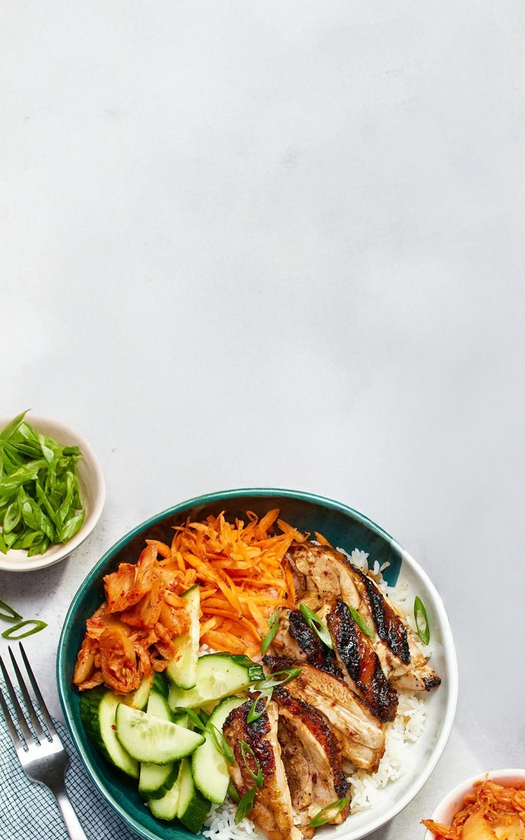 Bowl of salad with grilled chicken, carrots, and cucumbers on a white background