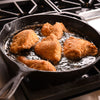A cast iron skillet filled with hot oil and fried chicken.