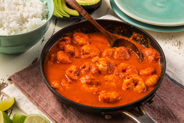 A close-up of a pan of shrimp in a red sauce with a wooden spoon.