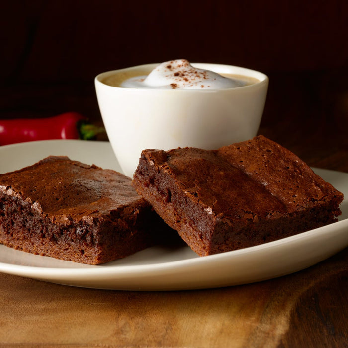 Two brownies on a white plate next to a cup of cappuccino.