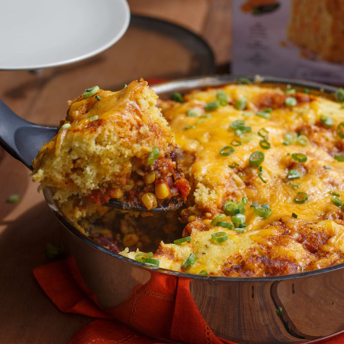 A close-up of a casserole dish with a cheesy cornbread topping and a scoop of the casserole on a spatula.