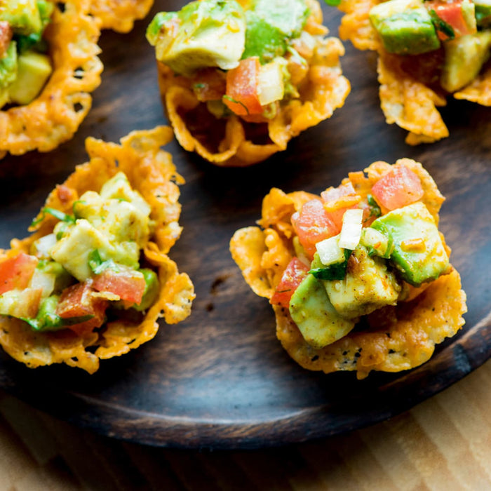 A close-up of four small bowls of avocado salsa, made with crispy cheese shells.