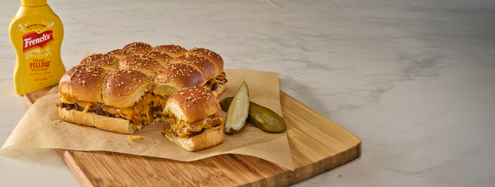 Burger sliders on a wooden board with a bottle of mustard in the background