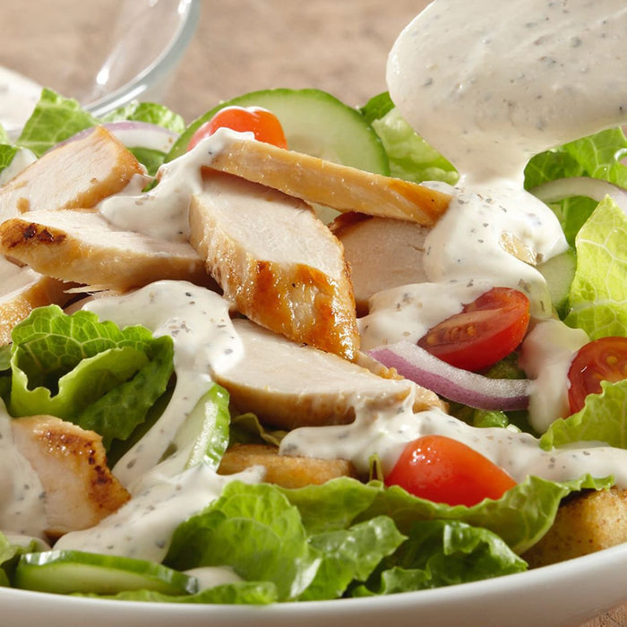A close-up of a salad with grilled chicken, cucumbers, tomatoes, red onion, and a creamy dressing.