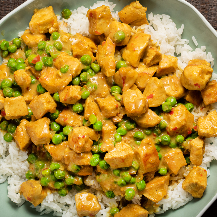 A close-up of a bowl of chicken curry with peas and rice.