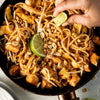 A close-up of a plate of Pad Thai noodles with chicken, peanuts, bean sprouts, and a lime wedge.