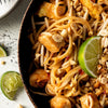 A close-up of a plate of Pad Thai noodles with chicken, peanuts, bean sprouts, and a lime wedge.