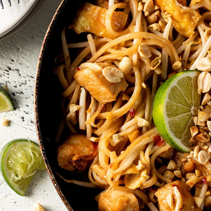 A close-up of a plate of Pad Thai noodles with chicken, peanuts, bean sprouts, and a lime wedge.