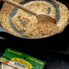 A close up of a cast iron skillet with sesame seeds being toasted with a wooden spoon, and a bag of El Guapo sesame seeds.