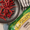 A package of El Guapo Arbol Chile Pods sits next to a pan of dried red chili peppers.