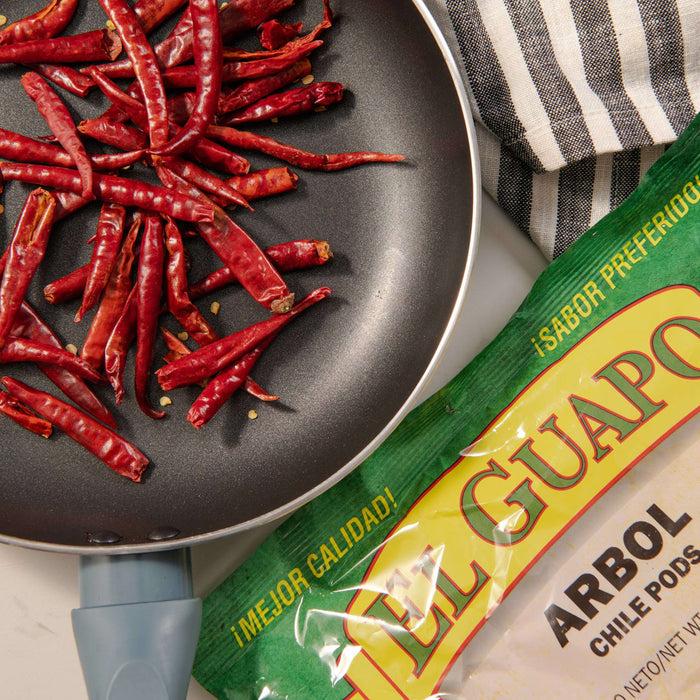 A package of El Guapo Arbol Chile Pods sits next to a pan of dried red chili peppers.