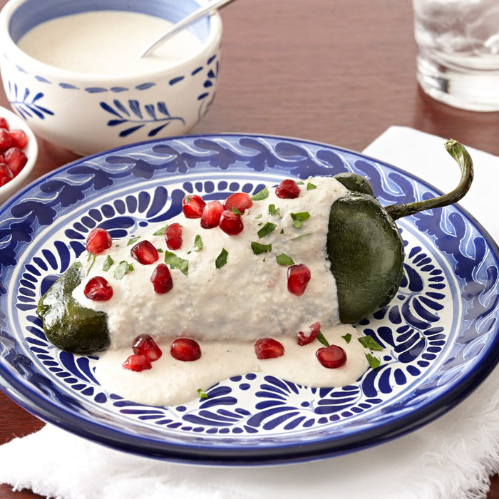 A plate of chiles rellenos topped with a creamy sauce and pomegranate seeds.