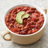 A bowl of chili topped with avocado slices.