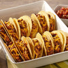 A white baking dish filled with mini tacos topped with shredded cheese.