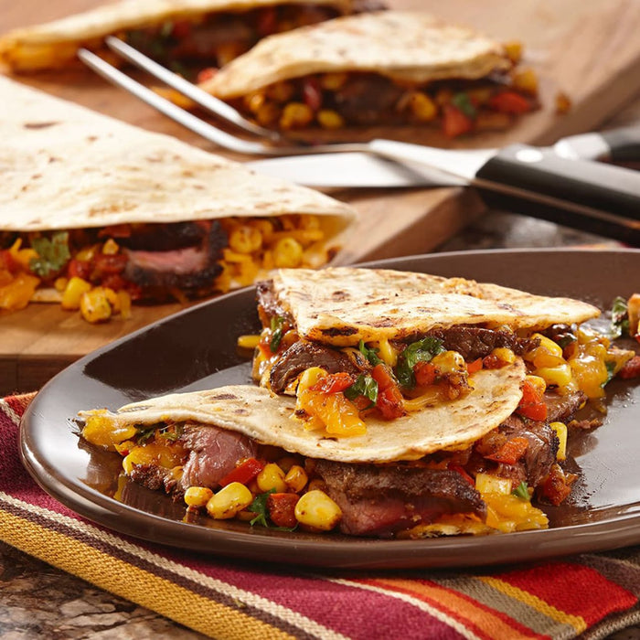 A plate of steak quesadillas with corn, peppers, and cheese.