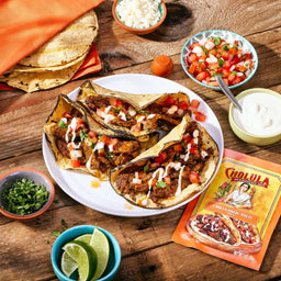 A plate of tacos with toppings and a packet of Cholula Chili Garlic Taco Seasoning Mix.