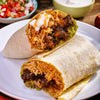 Two delicious burritos, likely seasoned with Cholula Chili Gar Taco Seas Mix 1 Oz, are presented on a white plate with salsa and sour cream in the background