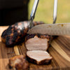 A close-up of a grilled pork tenderloin being sliced with a knife.