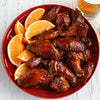 A red bowl filled with barbecue chicken wings and orange slices.