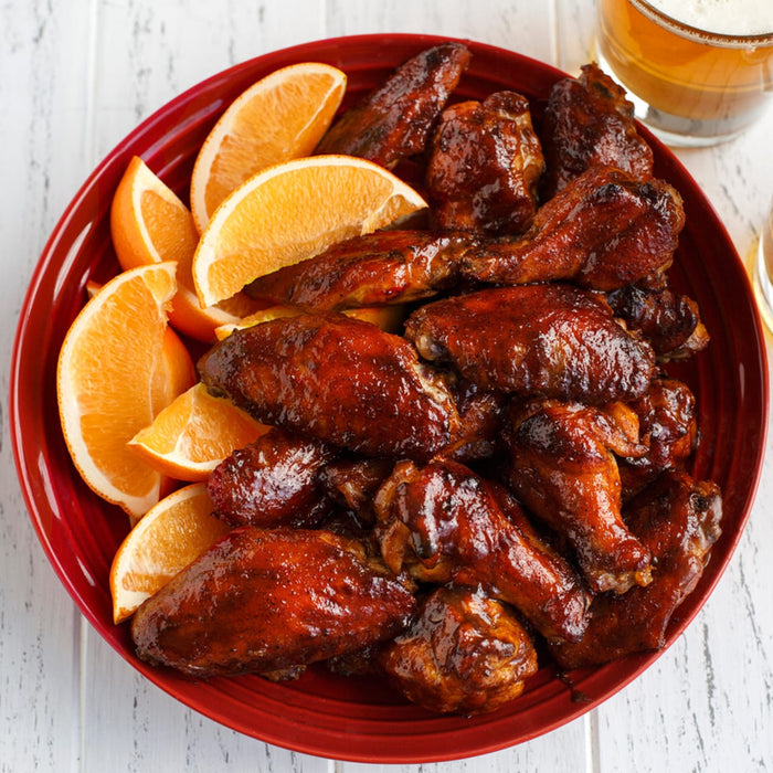 A red bowl filled with barbecue chicken wings and orange slices.