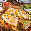 A close-up of a cheesy quesadilla cut into slices, topped with green onions and served on a wooden board.