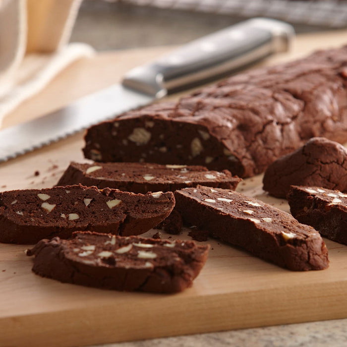 Chocolate biscotti with white chocolate chips are sliced on a wooden cutting board.