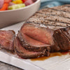 A close-up of a sliced grilled steak on a white plate.
