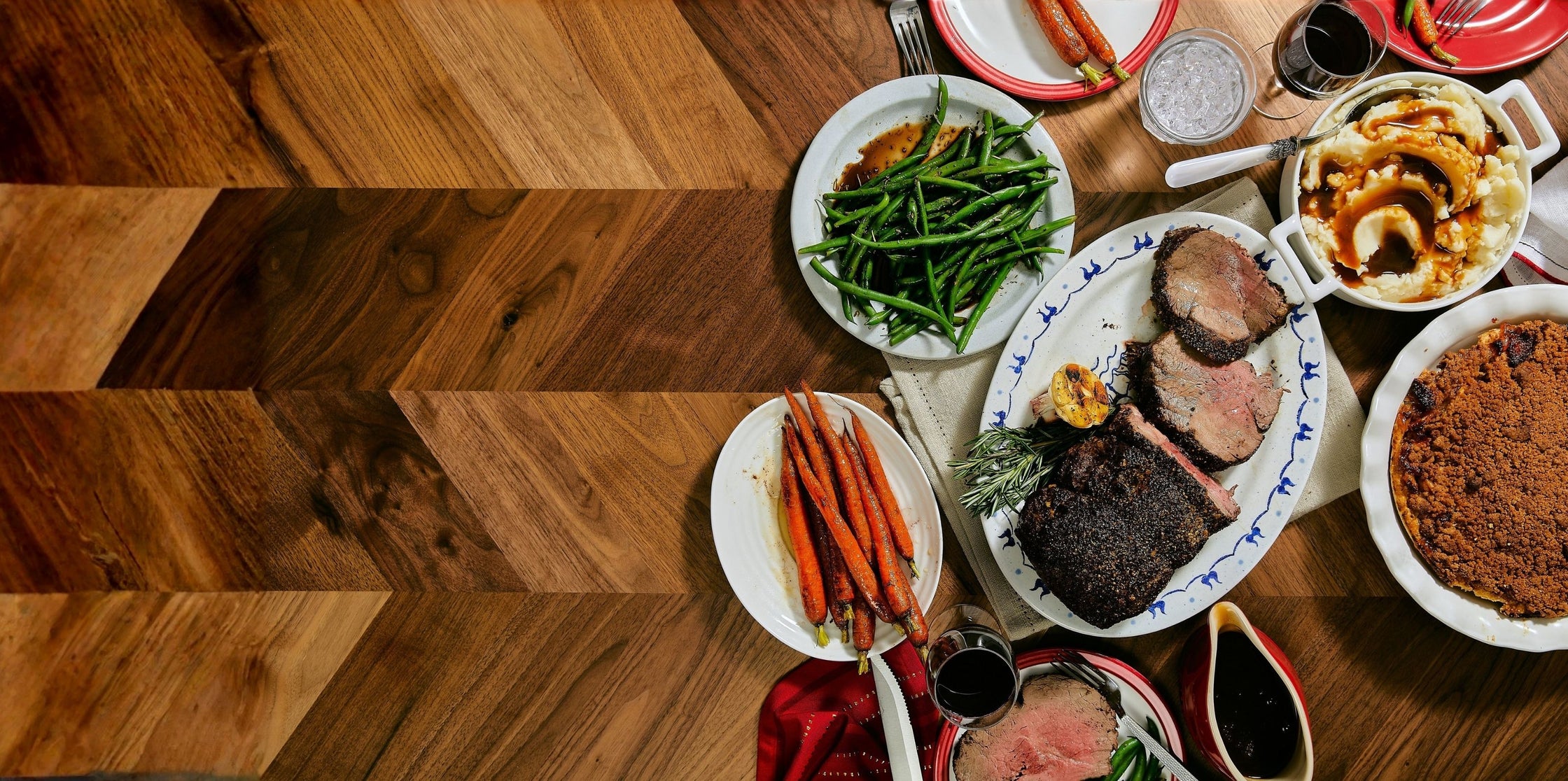 Dinner table set with various dishes including meat, vegetables, and sides on a wooden floor.