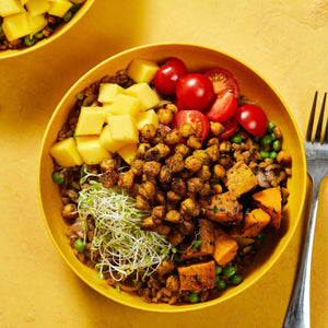 A yellow bowl filled with a colorful and healthy salad with chickpeas, sweet potatoes, mango, tomatoes, and sprouts.