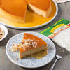 A slice of flan topped with coconut flakes on a blue and white patterned plate next to a bag of El Guapo coconut flakes.